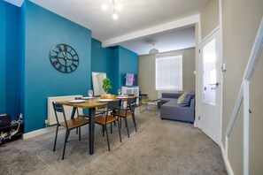A dining area with a table and chairs, a clock on the wall, and a television in the background. - Two-Bedroom Townhouse (Vale of Glamorgan)
