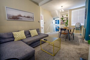 A living room with a grey sofa, a coffee table, and a dining area with a table and chairs. - Two-Bedroom Townhouse (Vale of Glamorgan)