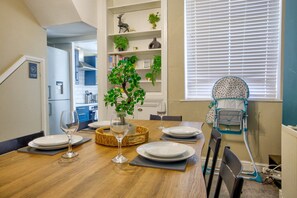 A dining area with a wooden table set for four, a vase with a plant, and a baby high chair. - Two-Bedroom Townhouse (Vale of Glamorgan)