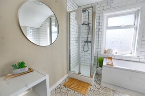 Une salle de bain avec une douche à parois de verre, un miroir rond, un lavabo blanc et une fenêtre donnant sur un beau paysage.