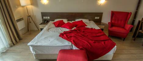 A hotel room with a bed, a red armchair, a red ottoman, a bedside table with a lamp, and a wall-mounted phone.