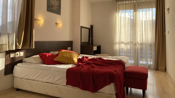 Una habitación de hotel con cama, mesita de noche, lámpara, espejo y ventana con cortinas.