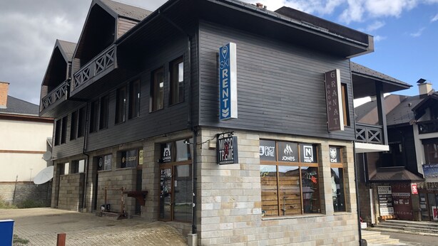 Un edificio con un cartel de alquiler de esquíes, una fachada comercial con varios rótulos y una apariencia de piedra.