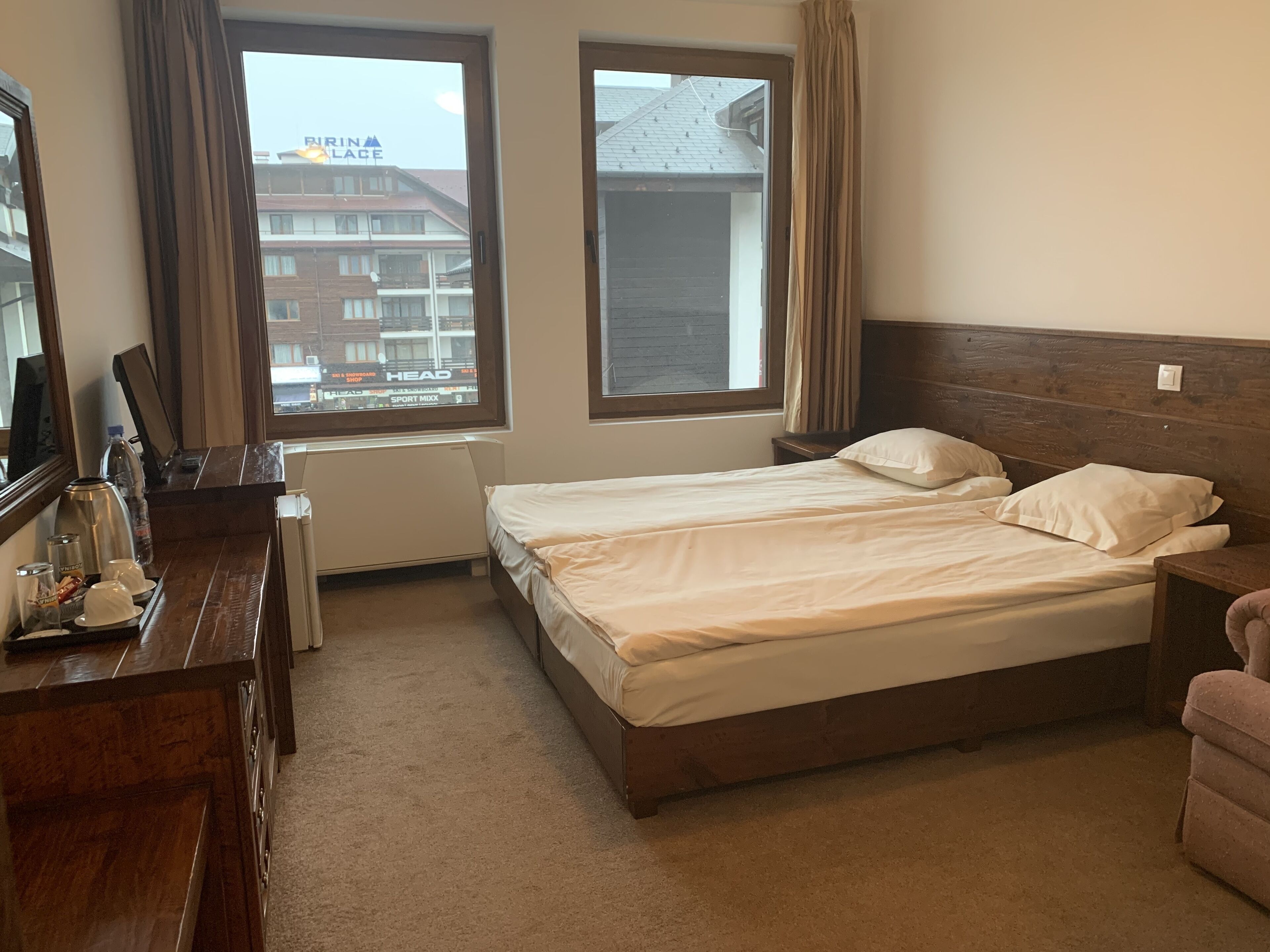 A hotel room with a bed, a desk with a coffee maker, and a view of a building with a sign.