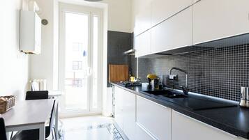 Eine moderne Küche mit weißen Schränken, einer schwarzen Arbeitsplatte und einer schwarzen Spritzschutzwand. Es gibt einen Essbereich mit Tisch und Stühlen sowie einen gemusterten Teppich auf dem Boden.