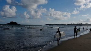 A beach with people walking and surfing, a clear sky, and distant land. - Happy hammocks, Weligama (Weligama)