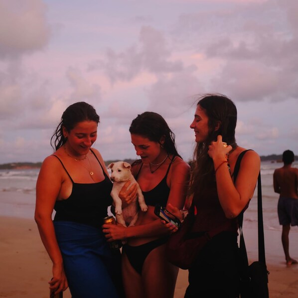 Tres personas en la playa con un perro, una sosteniendo una bebida.