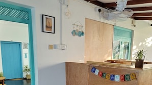 A reception desk with a potted plant, a blue door, and a wall-mounted fan. - Happy hammocks, Weligama (Weligama)