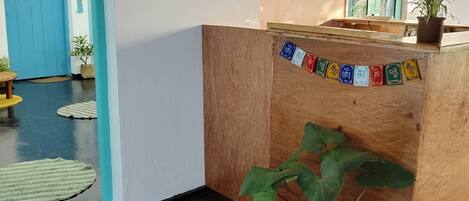 Una mesa de recepción con una planta en maceta, una puerta azul y un ventilador fijado a la pared.