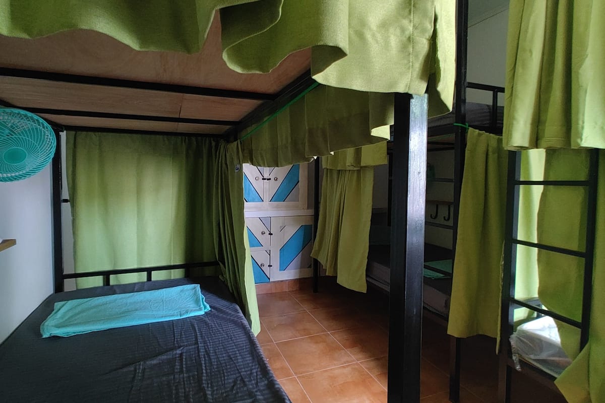 Une chambre de dortoir avec des lits superposés, des rideaux verts et un sol carrelé.