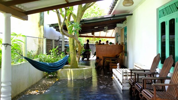 A covered outdoor area with a hammock, wooden chairs, and a concrete planter with a tree. - Happy hammocks, Weligama (Weligama)