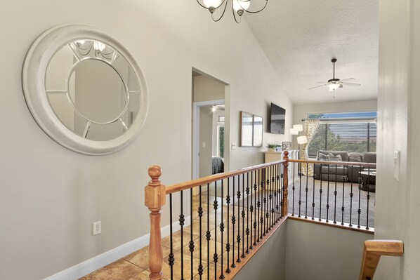 A staircase with a wooden handrail and black balusters leading to a living area with a gray sofa and a ceiling fan.