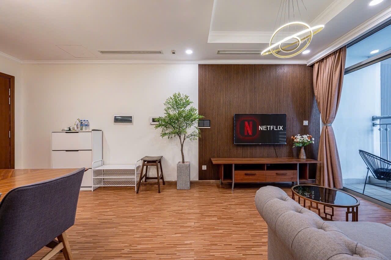 A modern living room with a wooden floor, a sofa, a TV mounted on a wooden wall, a small table, and a potted plant.