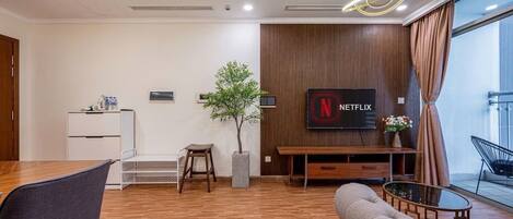 A modern living room with a wooden floor, a sofa, a TV mounted on a wooden wall, a small table, and a potted plant.