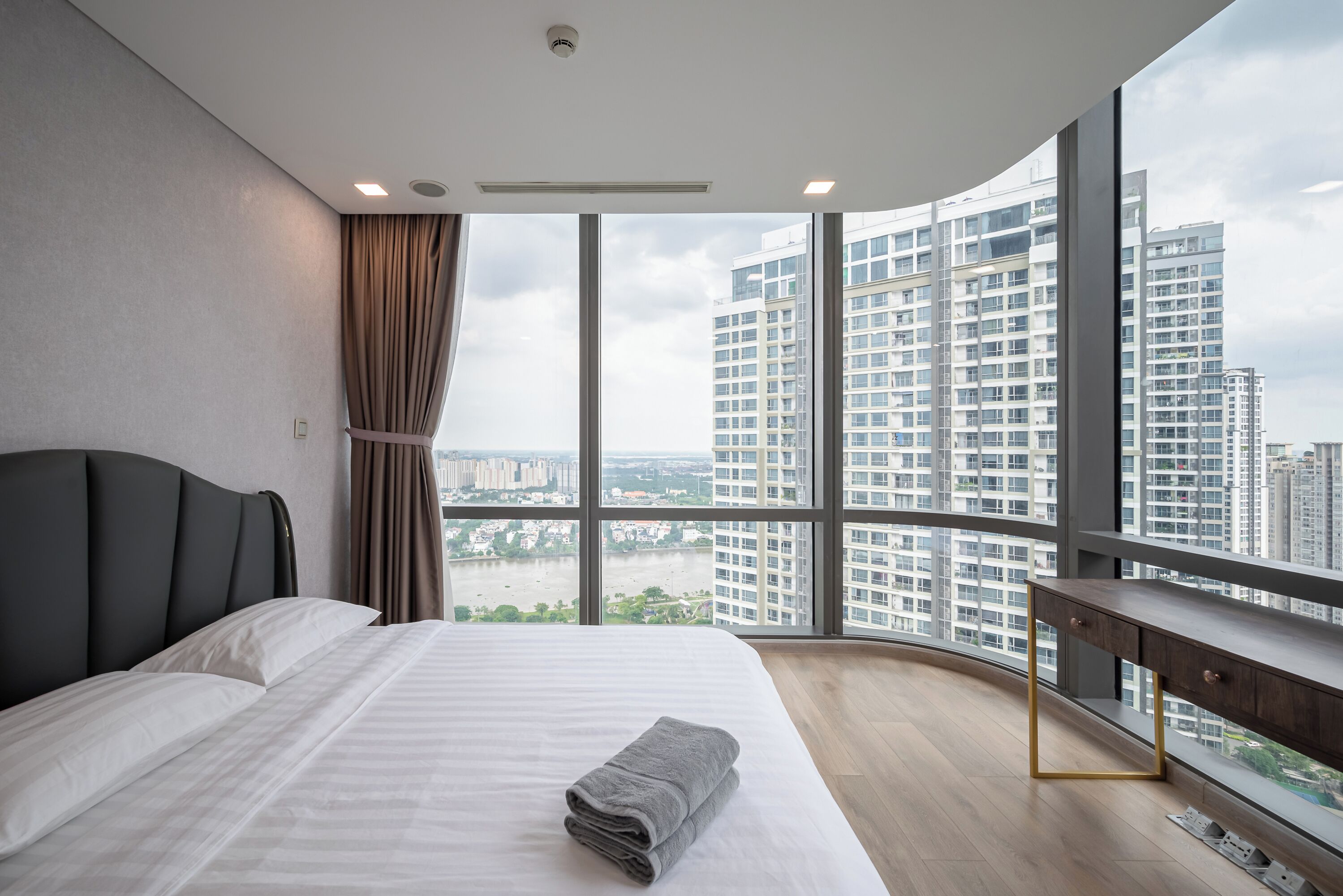A modern hotel room with a large bed, a desk, and a view of a cityscape.