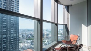 Une chambre située dans un immeuble de grande hauteur, dotée de grandes fenêtres, de deux fauteuils et offrant une vue sur le paysage urbain.