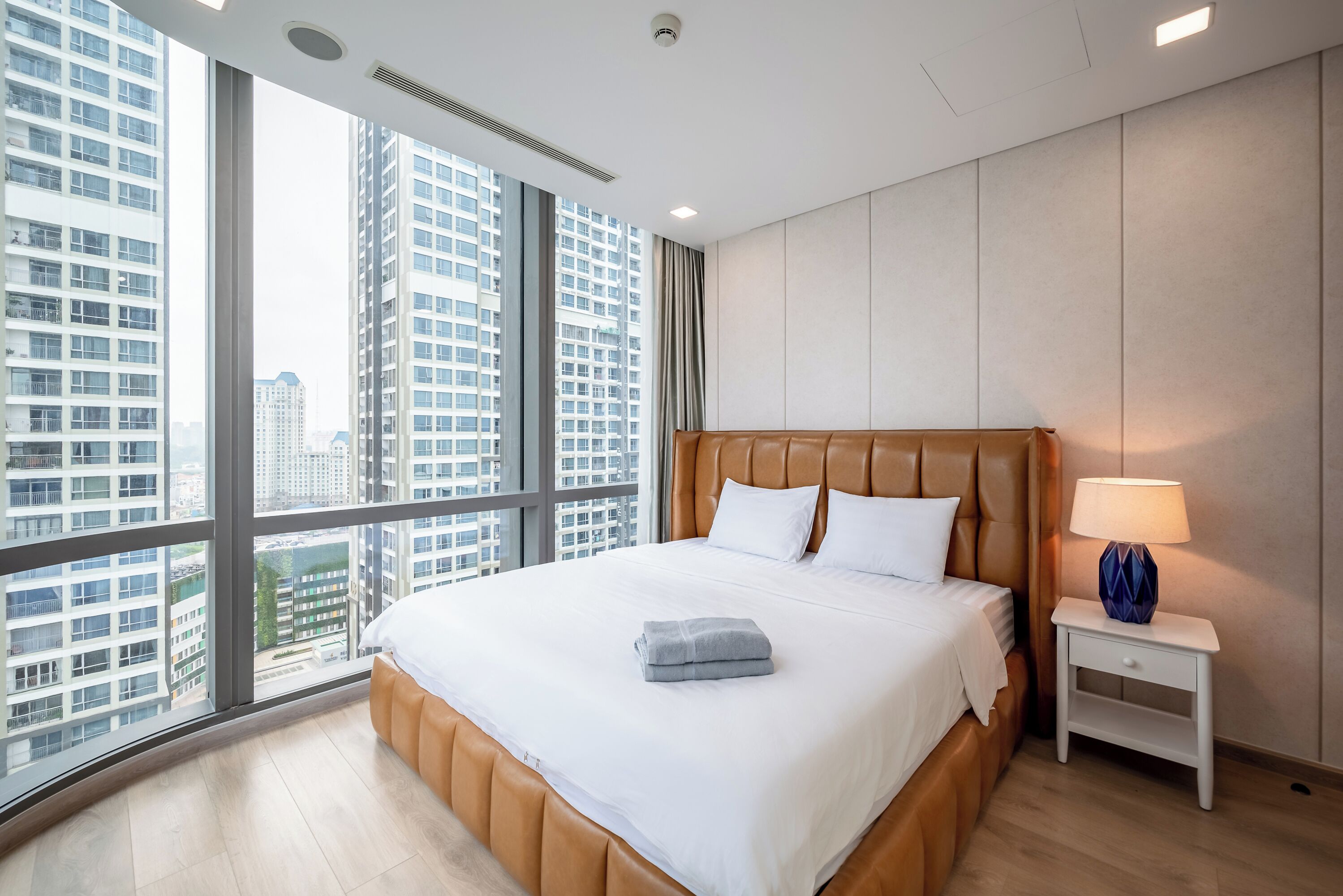 Une chambre d’hôtel moderne avec un grand lit, une table de chevet et une vue sur de hauts immeubles.
