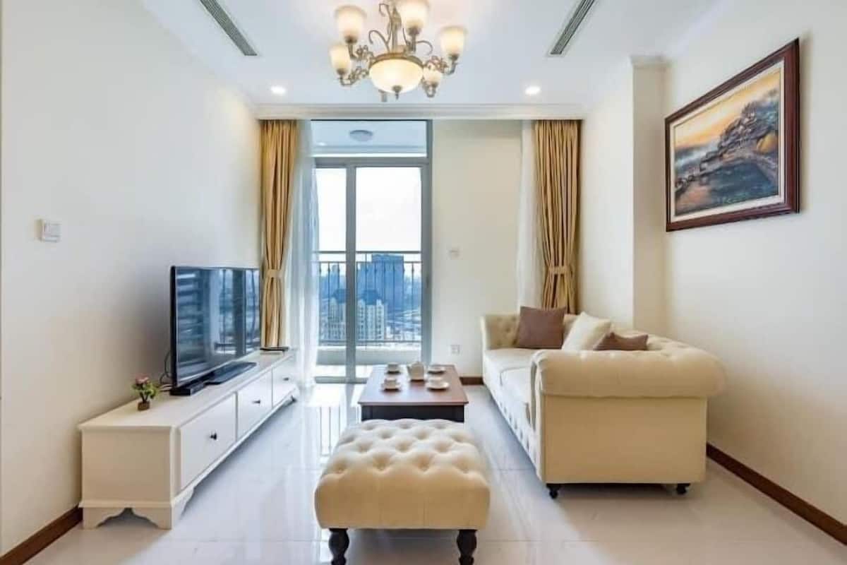 Una sala de estar moderna con un televisor de pantalla plana, un sofá color beige, una mesa de centro y una araña.