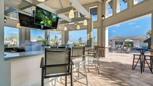Uma área de bar com televisão, cadeiras e vista para o oceano.