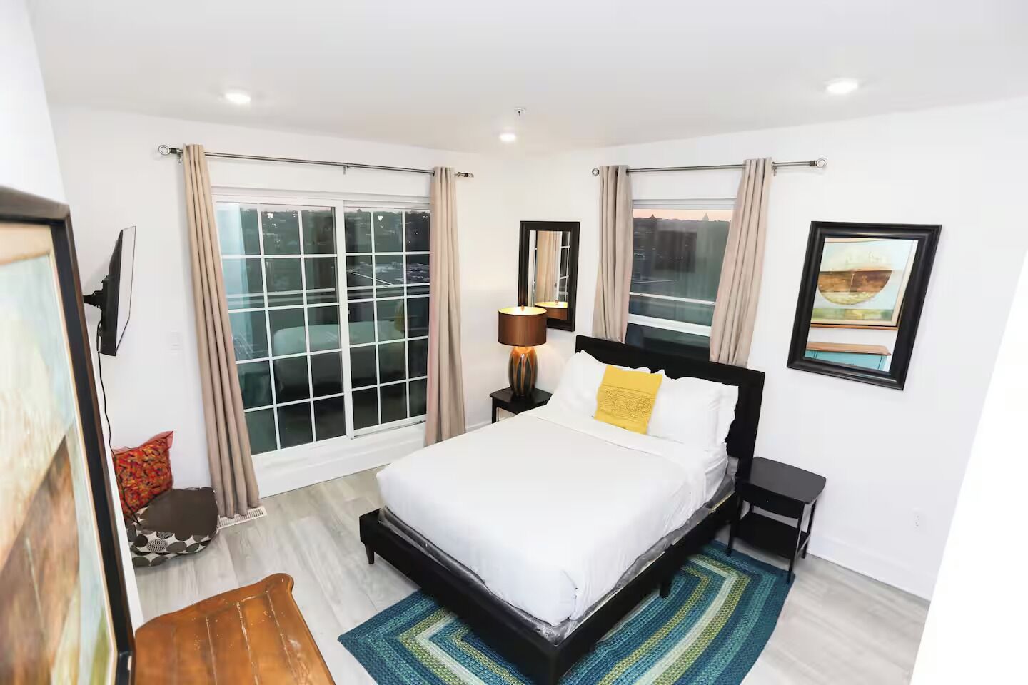 Ein Hotelzimmer mit einem großen Bett, einem Nachttisch, einer Lampe, einem Fernseher und einem Fenster mit Vorhängen.