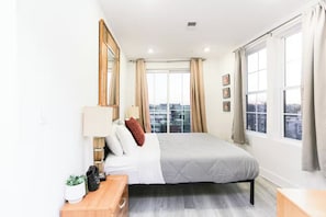 Une chambre moderne avec un lit, des tables de chevet, une fenêtre avec des rideaux et une vue sur la ville.