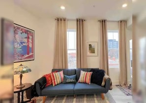 Un salon avec un canapé, une lampe et une vue sur la ville grâce à de grandes fenêtres.
