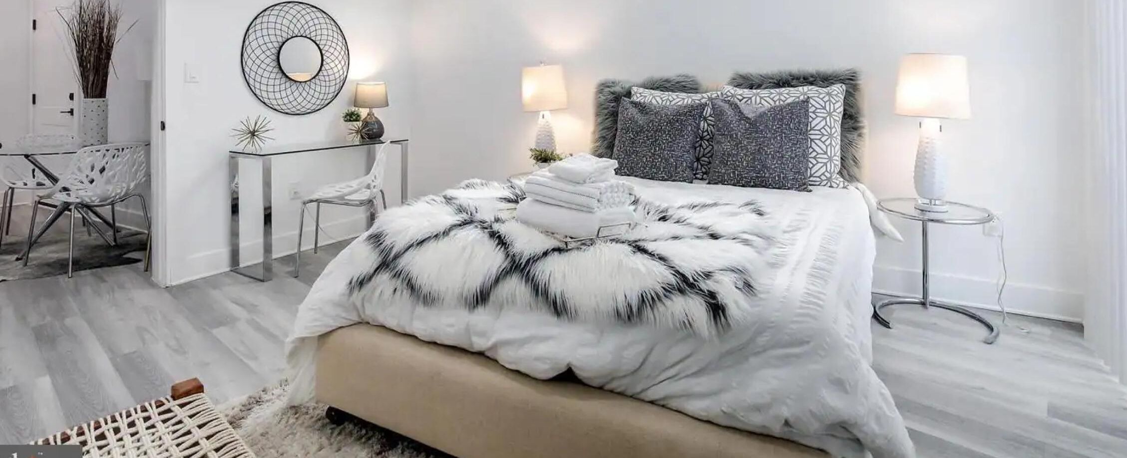 Ein modernes Schlafzimmer mit einem großen Bett, zwei Nachttischen, einem Spiegel und einem kleinen Tisch mit einer Lampe.