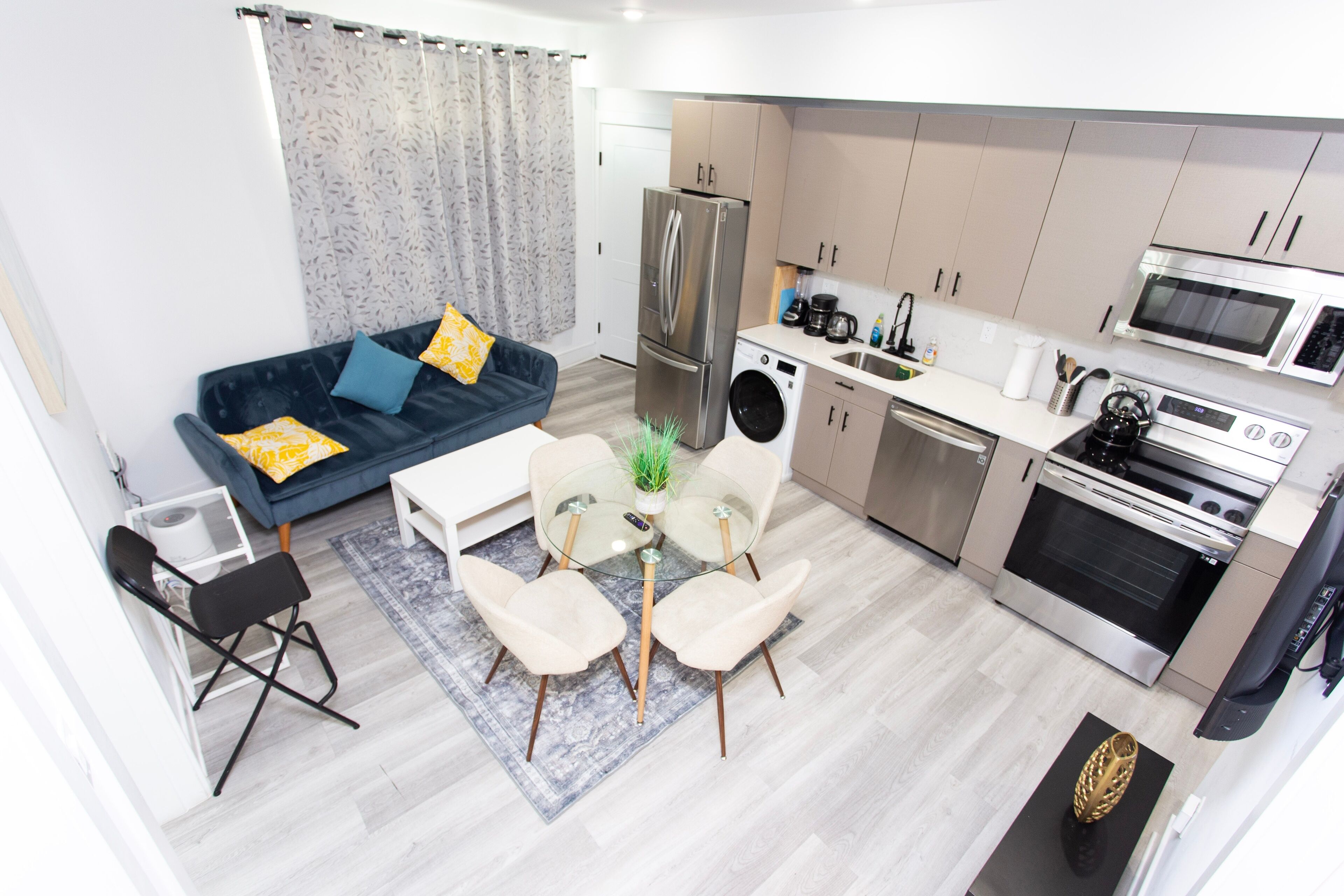 A compact living space with a sofa, dining table, chairs, a washing machine, a refrigerator, a microwave, and an oven.