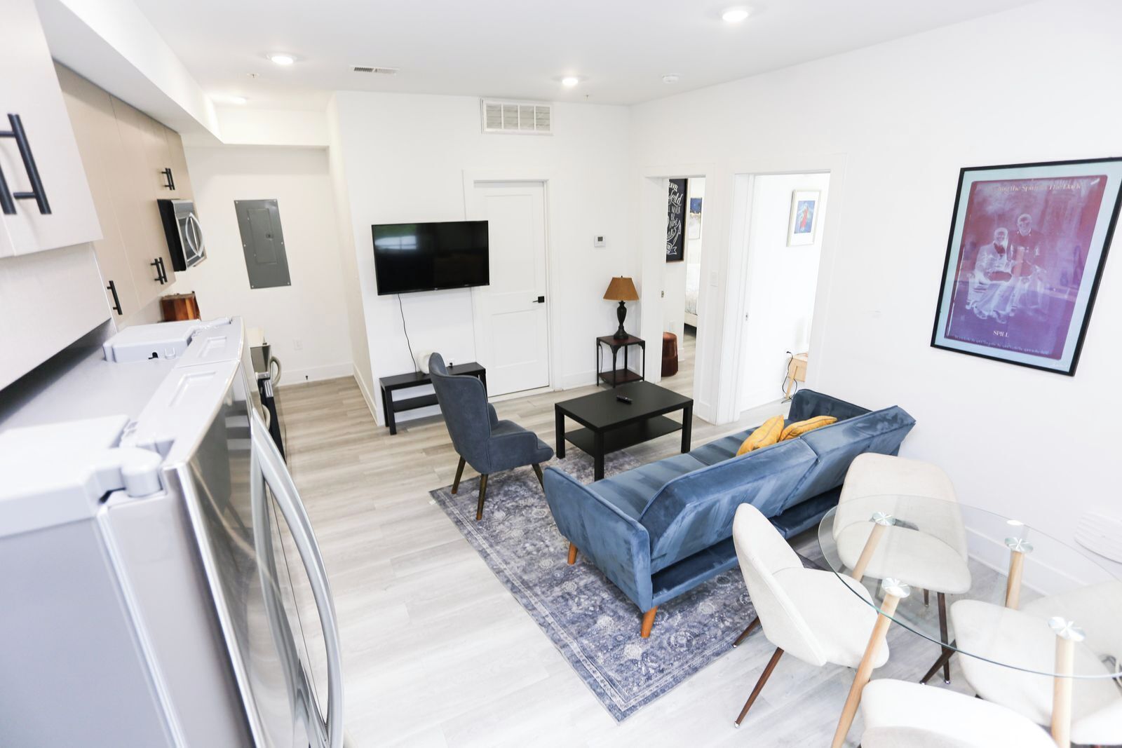 A modern living room with a sofa, chairs, a TV, and a kitchen area with appliances.