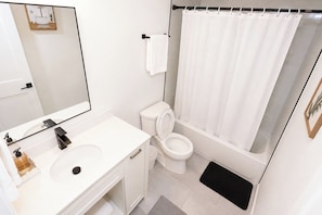 Et badeværelse med en hvid vask, toilet, badekar med bruseforhæng og et spejl.