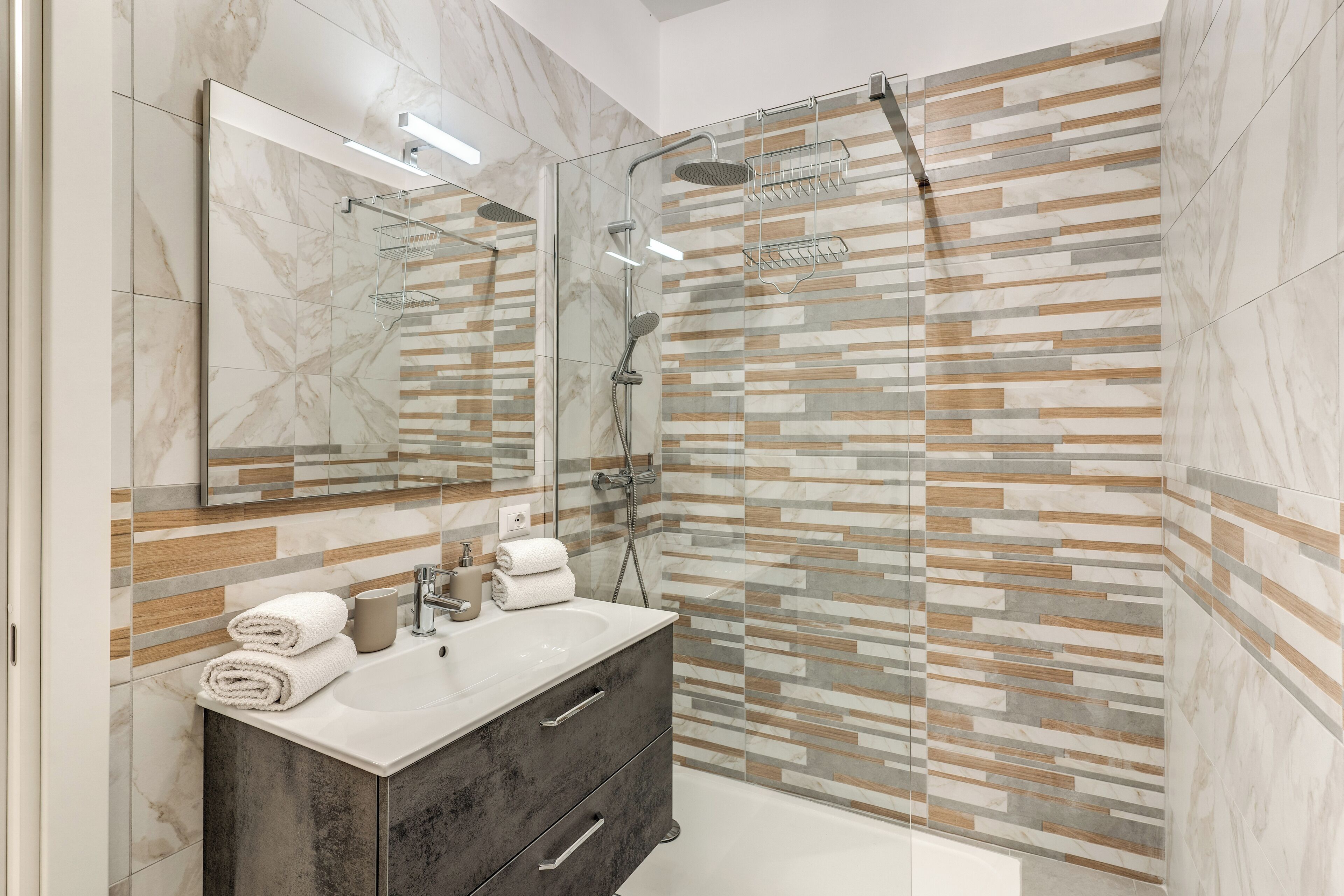 Un baño moderno con ducha envuelta en vidrio, tocador con azulejos de mármol y un espejo.