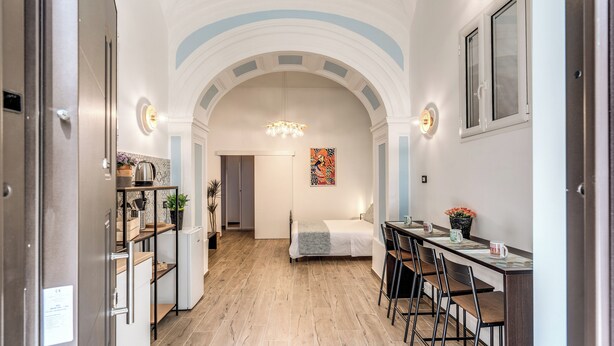 A modern kitchen with a built-in oven, a dining area with a long table and chairs, and a cozy bedroom with a bed and a nightstand. - The Quarters Naples Apartment (Naples)
