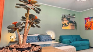 A room with a bed, a blue sofa, a potted plant, and a painting on the wall. - The Quarters Naples Apartment (Naples)