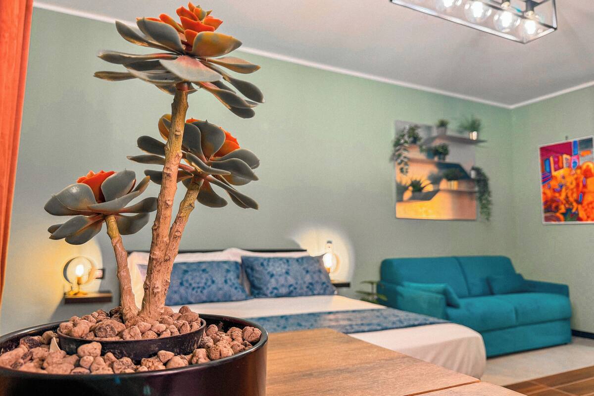 A room with a bed, a blue sofa, a potted plant, and a painting on the wall.