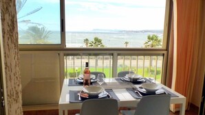 A dining table set for two with a view of the ocean and palm trees. - Comfortable apartment  with pool facing the sea (Six-Fours-les-Plages)