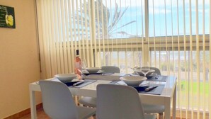 A dining area with a table set for four, white chairs, and a window with blinds. - Comfortable apartment  with pool facing the sea (Six-Fours-les-Plages)
