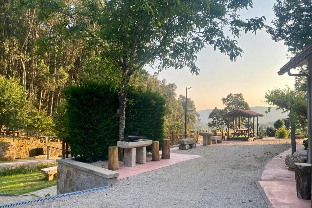 A serene outdoor area with a stone bench, a wooden gazebo, and a stone pathway.