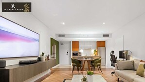 Ein modernes Wohnzimmer mit Flachbildfernseher, Essbereich mit Stühlen, Küche mit Schränken und einer Couch.
