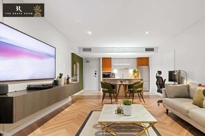 Un salon moderne doté d’un téléviseur à écran plat, d’un coin repas avec des chaises, d’une cuisine avec des placards et d’un canapé.