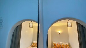 Reflejo de un dormitorio con dos camas, cada una con ropa de cama y almohadas estampadas, una pequeña mesa redonda y una alfombra con diseño.