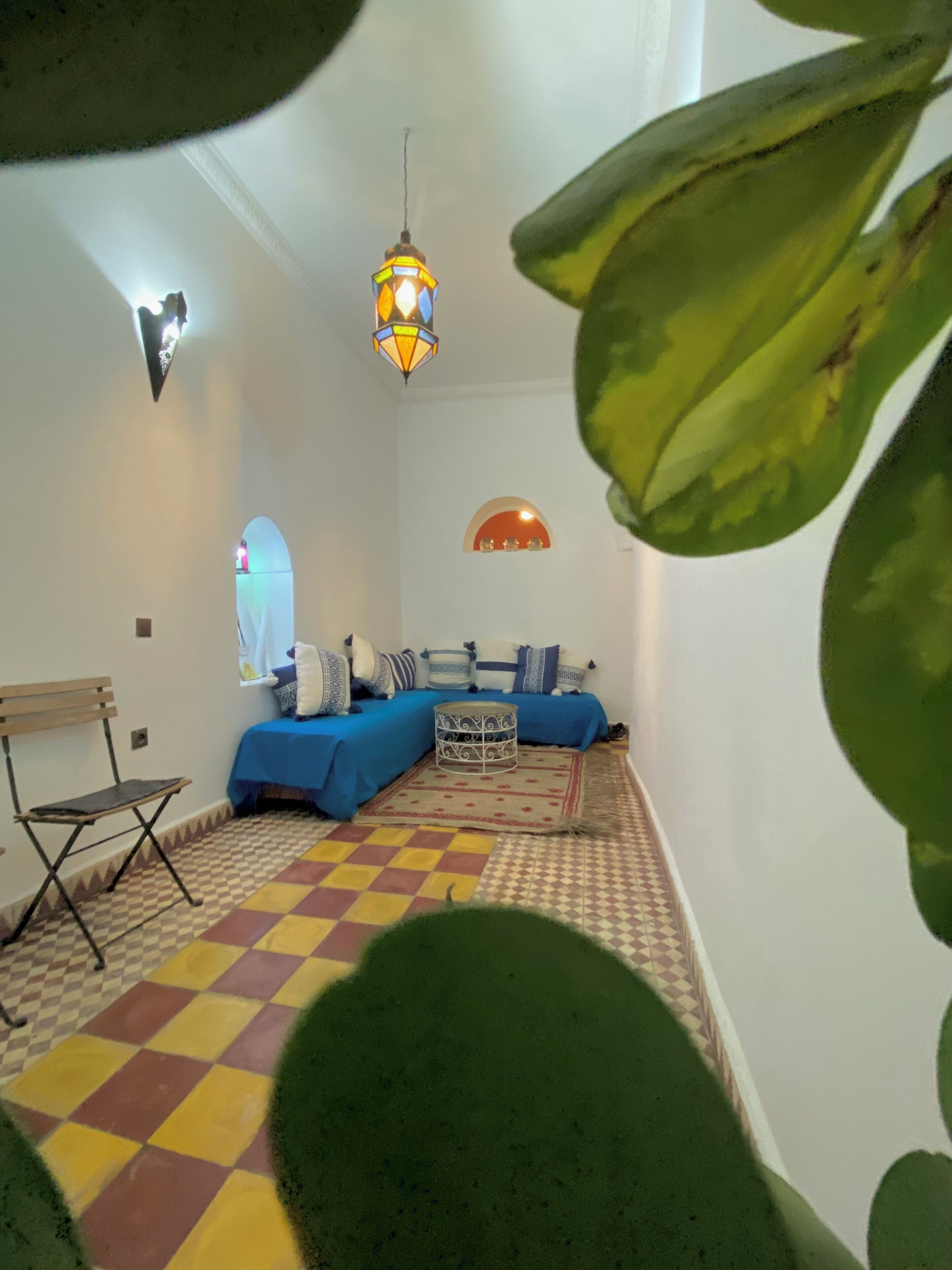 Een kamer met een zwart-wit schakeerdvloer, een blauwe zithoek, een kleine tafel en een hanglamp.