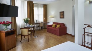 Una habitación de hotel con televisión de pantalla plana, zona de comedor con mesa y sillas, un sofá rojo y una cama.