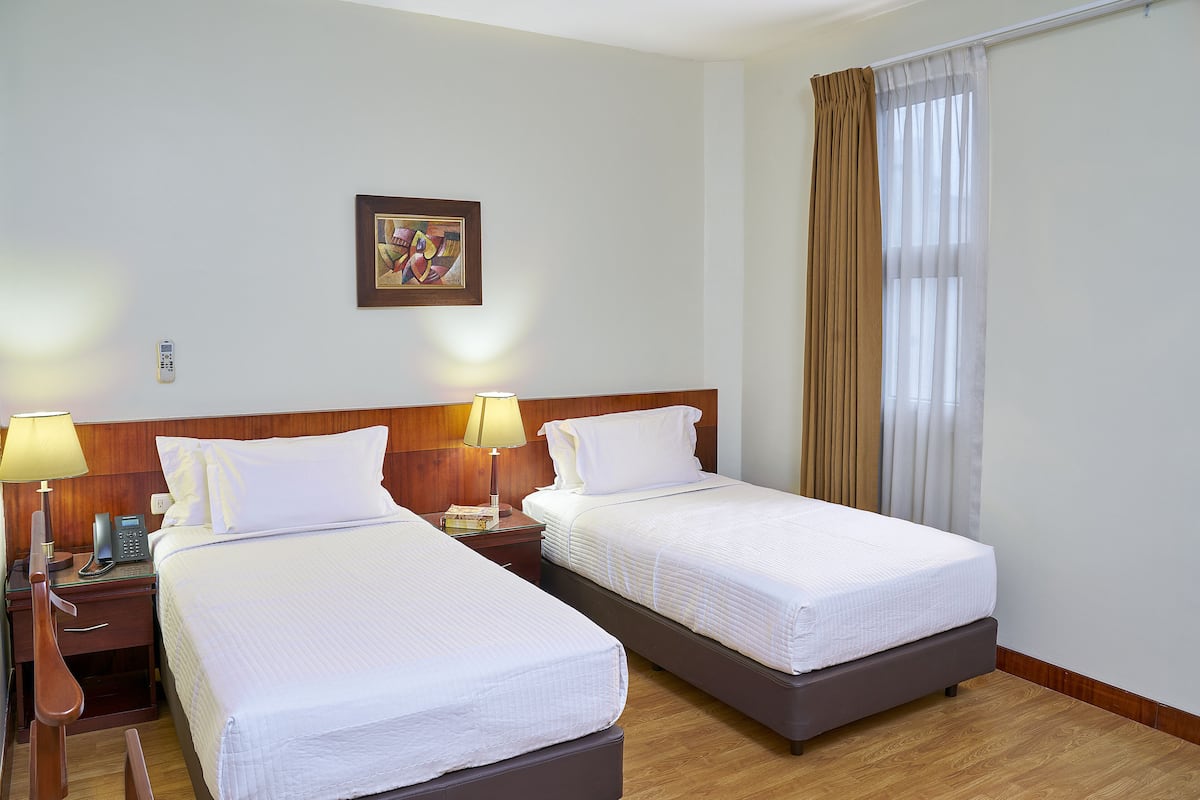 A hotel room with two single beds, a wooden headboard, a nightstand with a lamp, a telephone, and a framed picture on the wall.