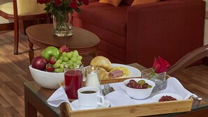 Habitación de hotel con una mesa de comedor dispuesta para el desayuno, un jarrón con rosas rojas y un cuadro en la pared.
