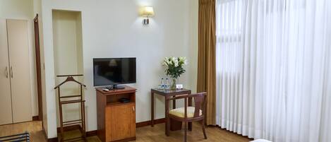 A hotel room with a bed, a TV, a desk with a chair, a wardrobe, and a window with curtains.