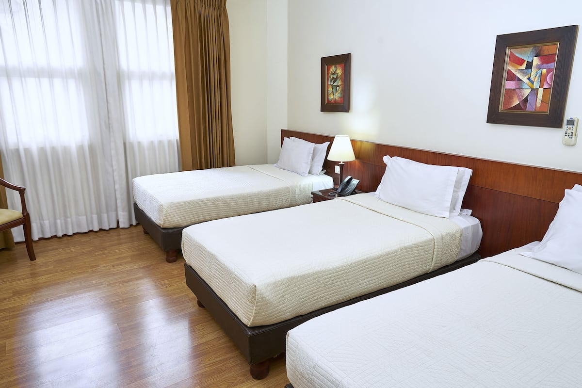 A hotel room with two beds, a wooden floor, a chair, and a window with curtains.