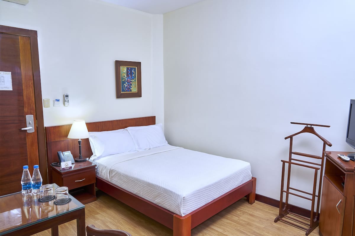 A neatly made hotel room with a bed, bedside table, lamp, and a hanging rack.