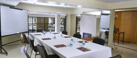 Una sala de conferencias con una larga mesa, sillas, botellas de agua y una pizarra.