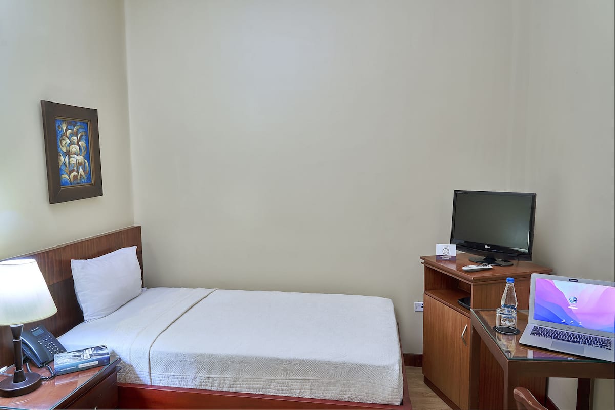 A hotel room with a bed, a desk with a laptop, a television, a phone, and a water bottle.