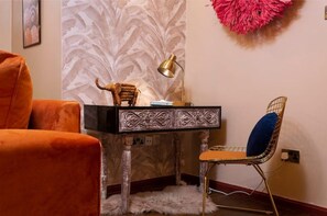 Canto de um quarto com uma escrivaninha, uma cadeira, um abajur e um enfeite de parede.